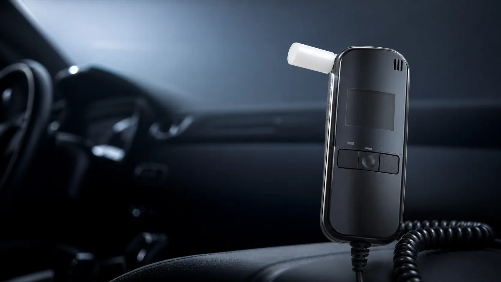 Handheld breathalyzer device with mouthpiece placed on a car interior surface.